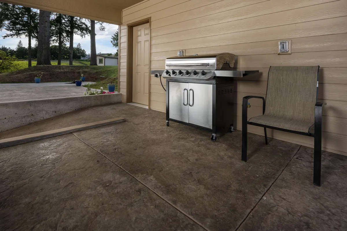 An inviting grill sits near a chair by a doorway, emphasizing the potential for casual barbecues and relaxed outdoor dining. The scene hints at easy access between indoor comfort and outdoor enjoyment.