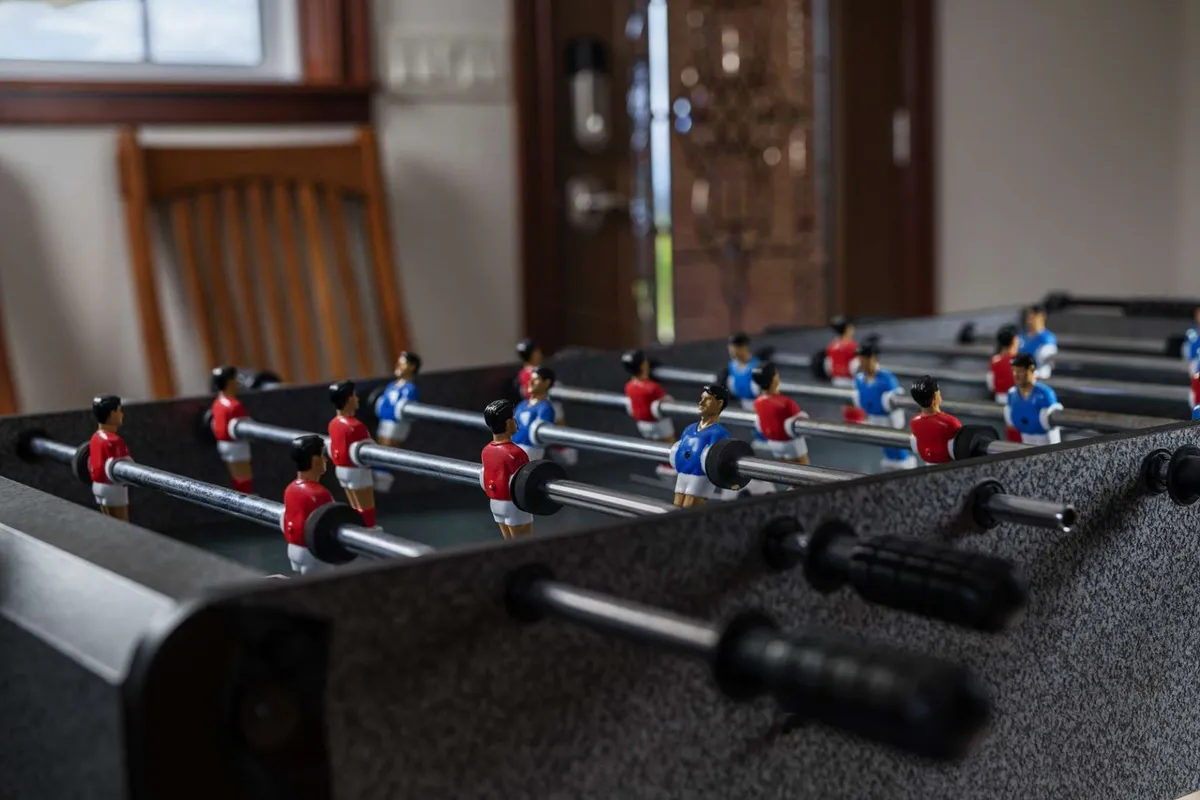 A foosball table set up in a vibrant communal space, featuring miniature players mid-game. The setting encourages playful interaction and social engagement, suggesting a hub for fun between excursions.
