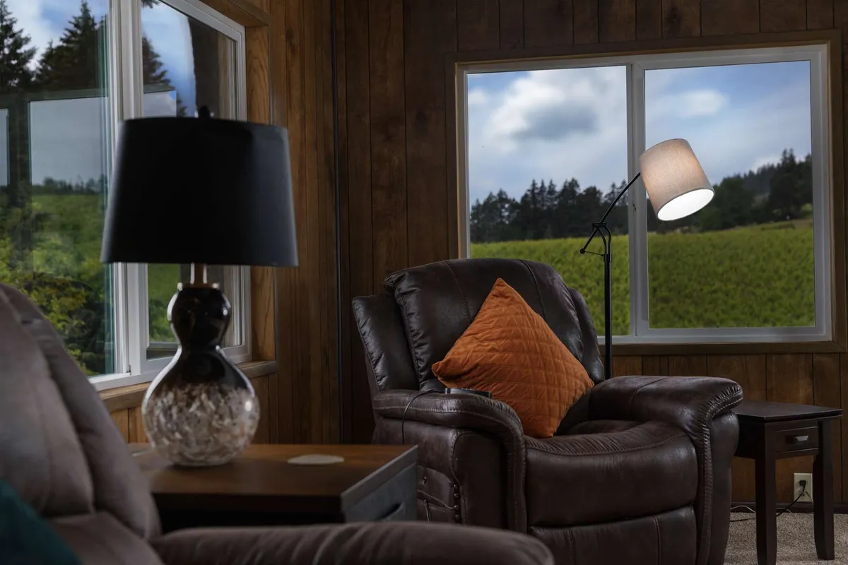 A cozy leather recliner with an orange decorative pillow sits beside a table lamp, positioned near a window that offers a tranquil view of the outdoors. The soft natural light and intimate setting evoke a sense of privacy and relaxation, making it ideal for unwinding or sharing a quiet moment together.