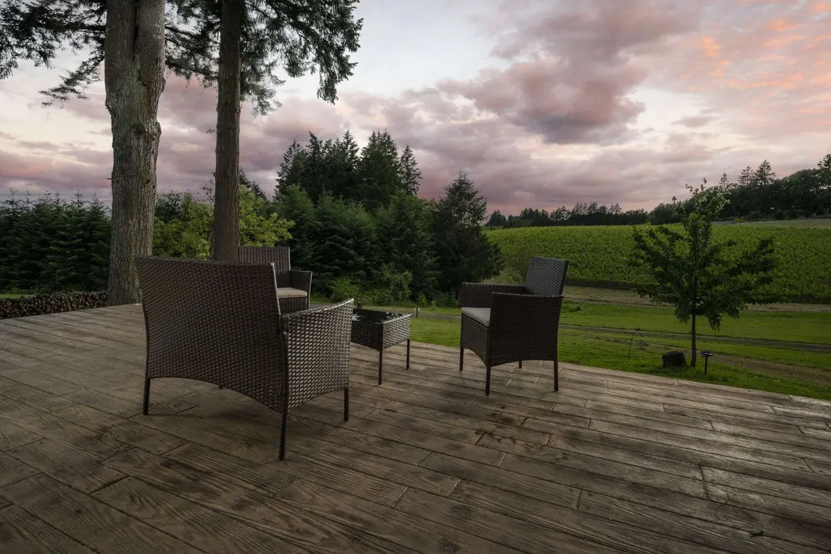 A serene outdoor seating area overlooks the vineyard landscape, with the sky painted in soft sunset hues. The setting invites relaxation and socializing while taking in the natural beauty and ambiance of the region.
