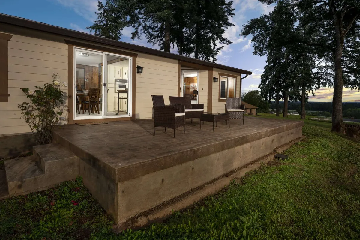 A serene outdoor patio set for dining, surrounded by lush greenery and with a view into an inviting indoor dining area. Comfortable chairs and ambient lighting create the ideal setting for sunset dinners or evening wine tastings.
